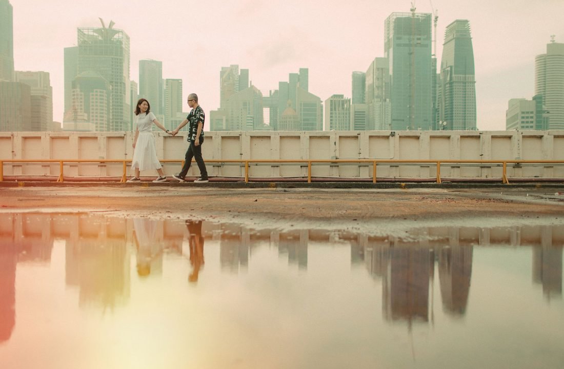 Couple walking hand-in-hand with Chinatown Singapore skyline and reflections