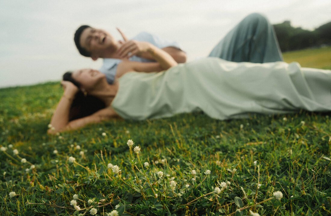 Theo and Kasey laughing while lying on grass at East Coast Park, Singapore