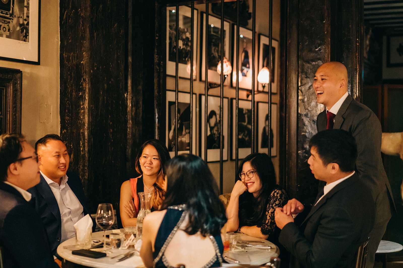 A group of friends and family enjoy a celebratory dinner at The English House Singapore, laughing and conversing around a table adorned with wine glasses and plates, capturing the joy of a Cacio e Pepe wedding reception.