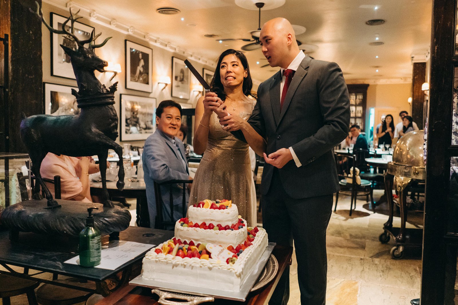 Couple cutting a wedding cake at The English House Wedding Singapore, with guests in the background.
