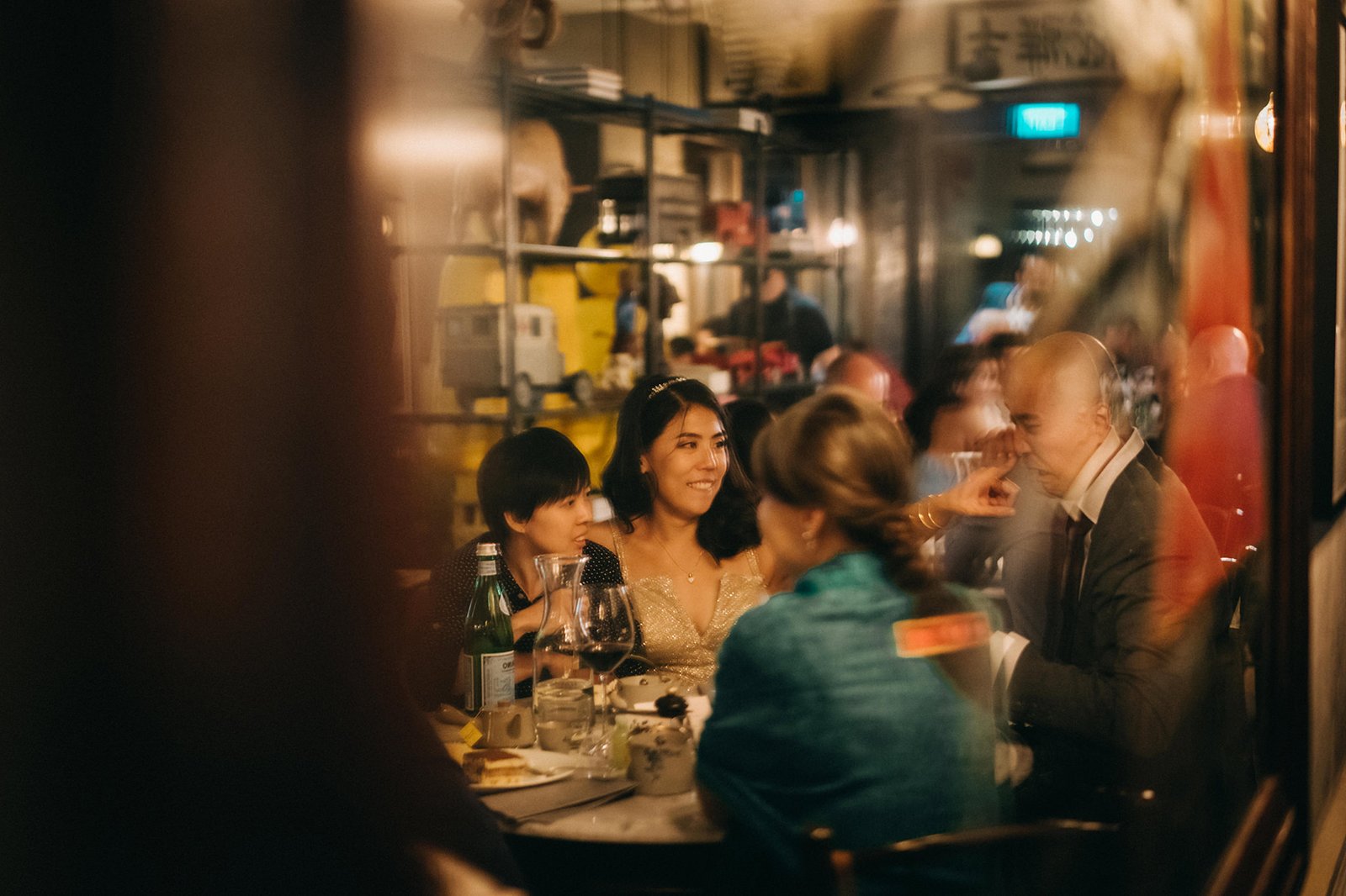 A wedding party enjoys a meal at The English House Singapore, with guests laughing and conversing around a table laden with food and wine.