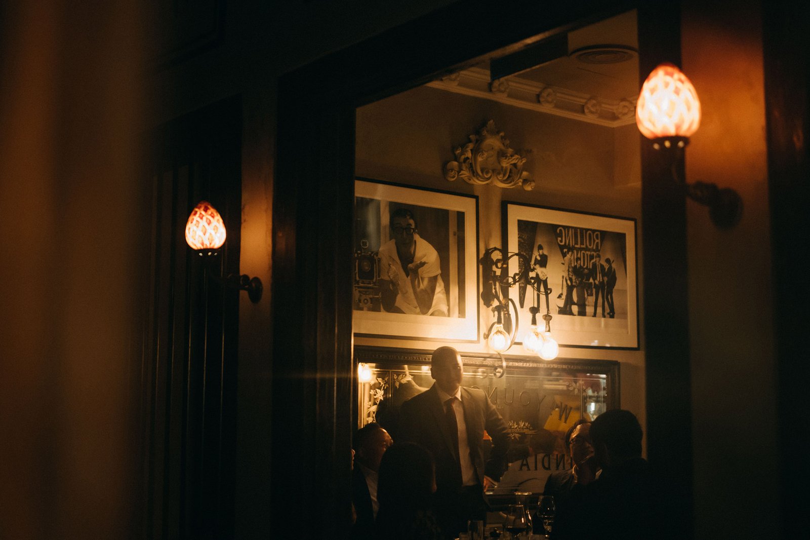 Elegant interior of The English House Singapore, with a man in a suit standing near framed photos and ornate lighting, evoking a sophisticated wedding reception atmosphere.
