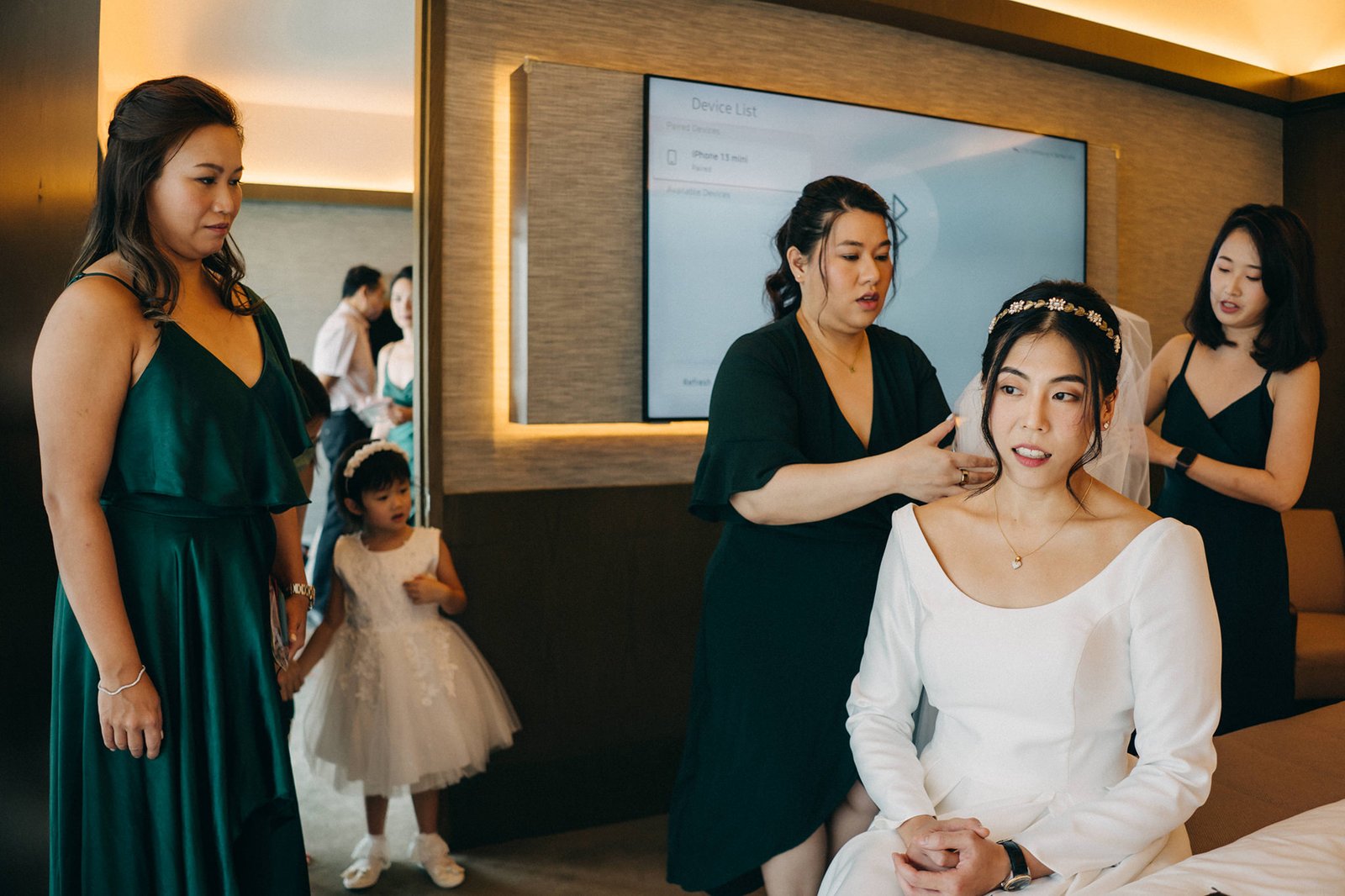 A bride in a white wedding dress and veil is being helped by a bridesmaid in a dark green dress, preparing for a Keyaki Garden Pavilion Wedding in Singapore.