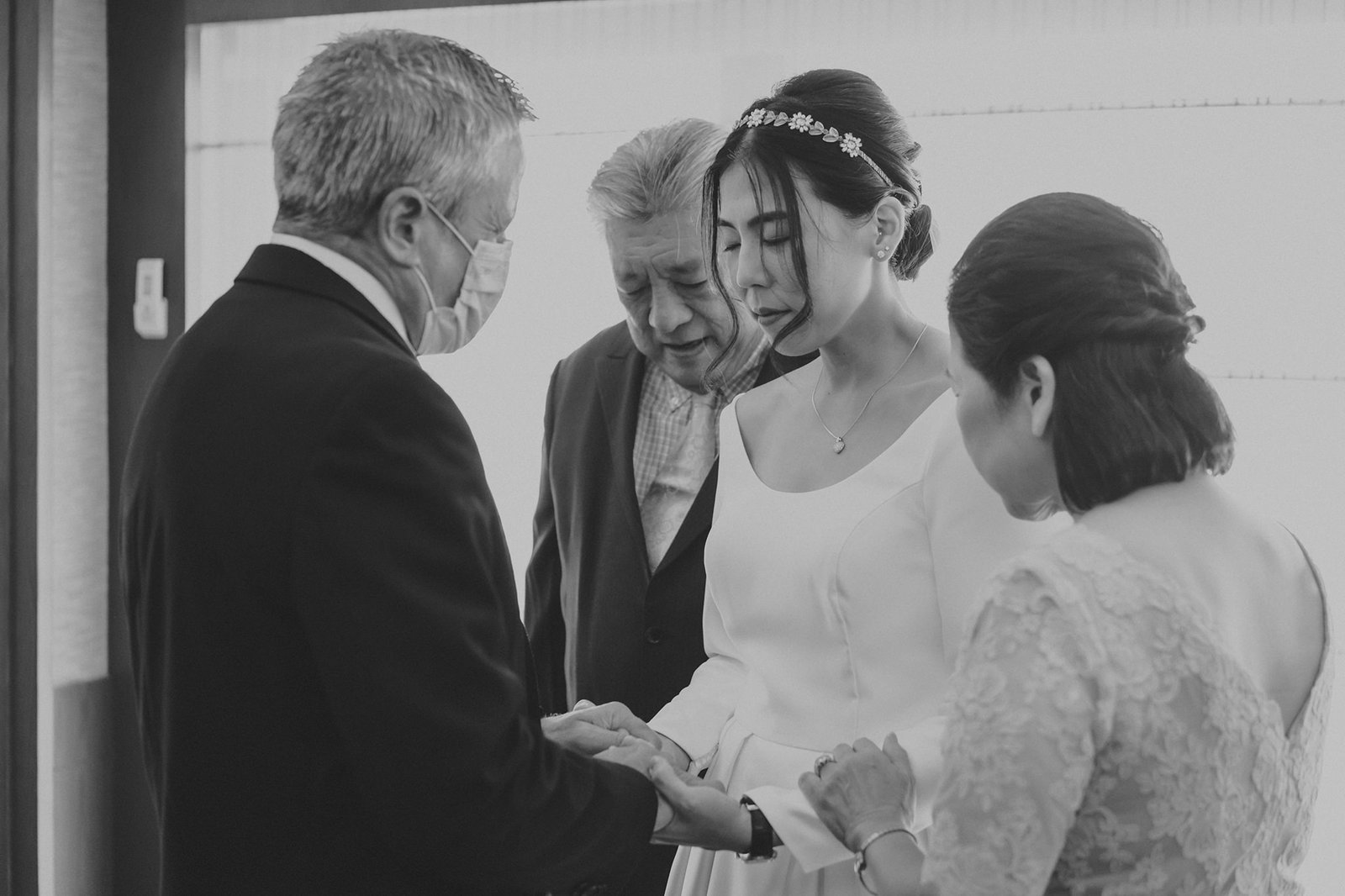 A bride in a wedding dress holds hands with her father at a Keyaki Garden Pavilion wedding in Singapore, while her parents look on with emotion.