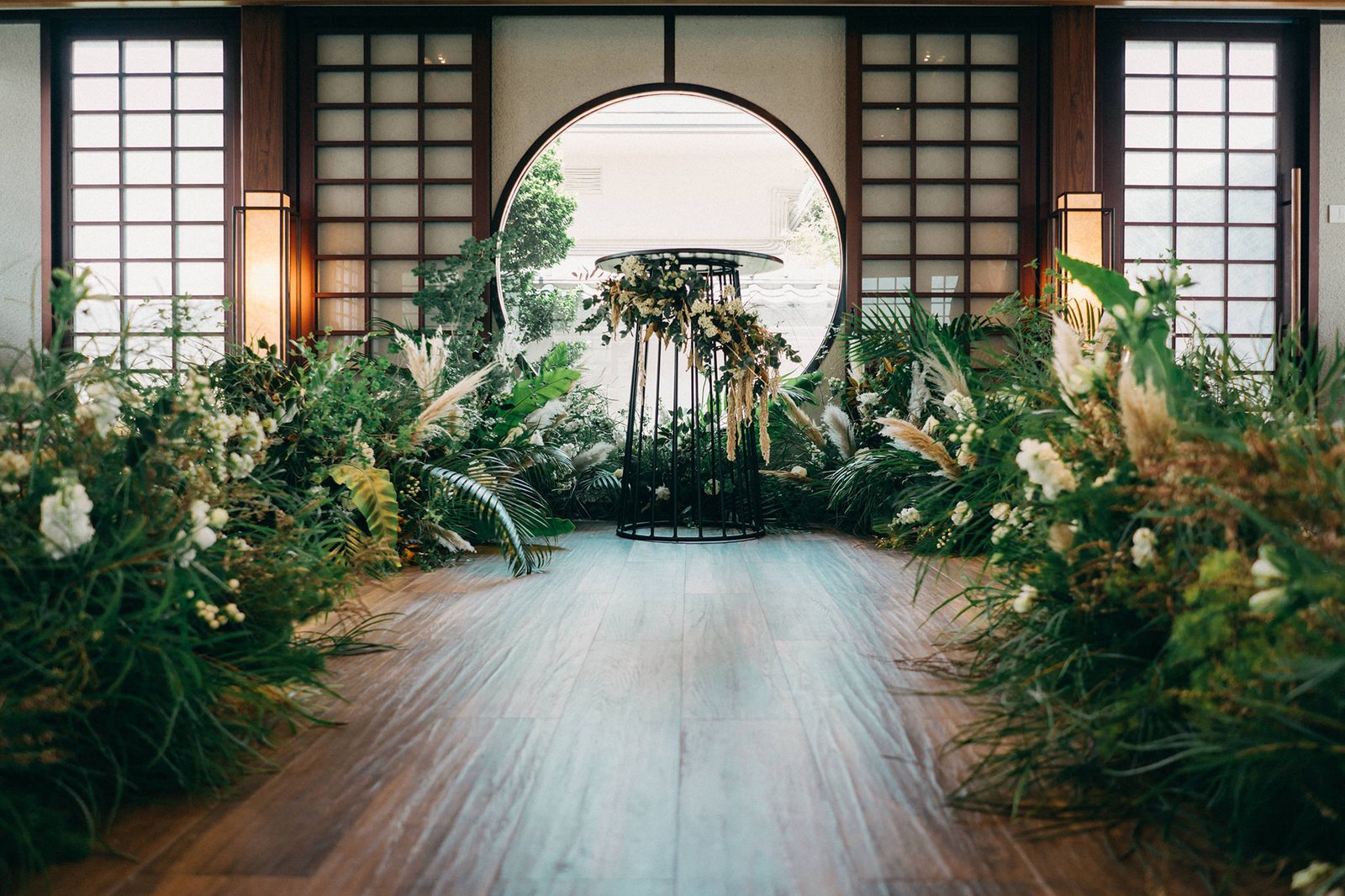 A romantic wedding aisle at the Keyaki Garden Pavilion Wedding Singapore, adorned with lush greenery, pampas grass, and white flowers, leading to a circular floral arrangement.