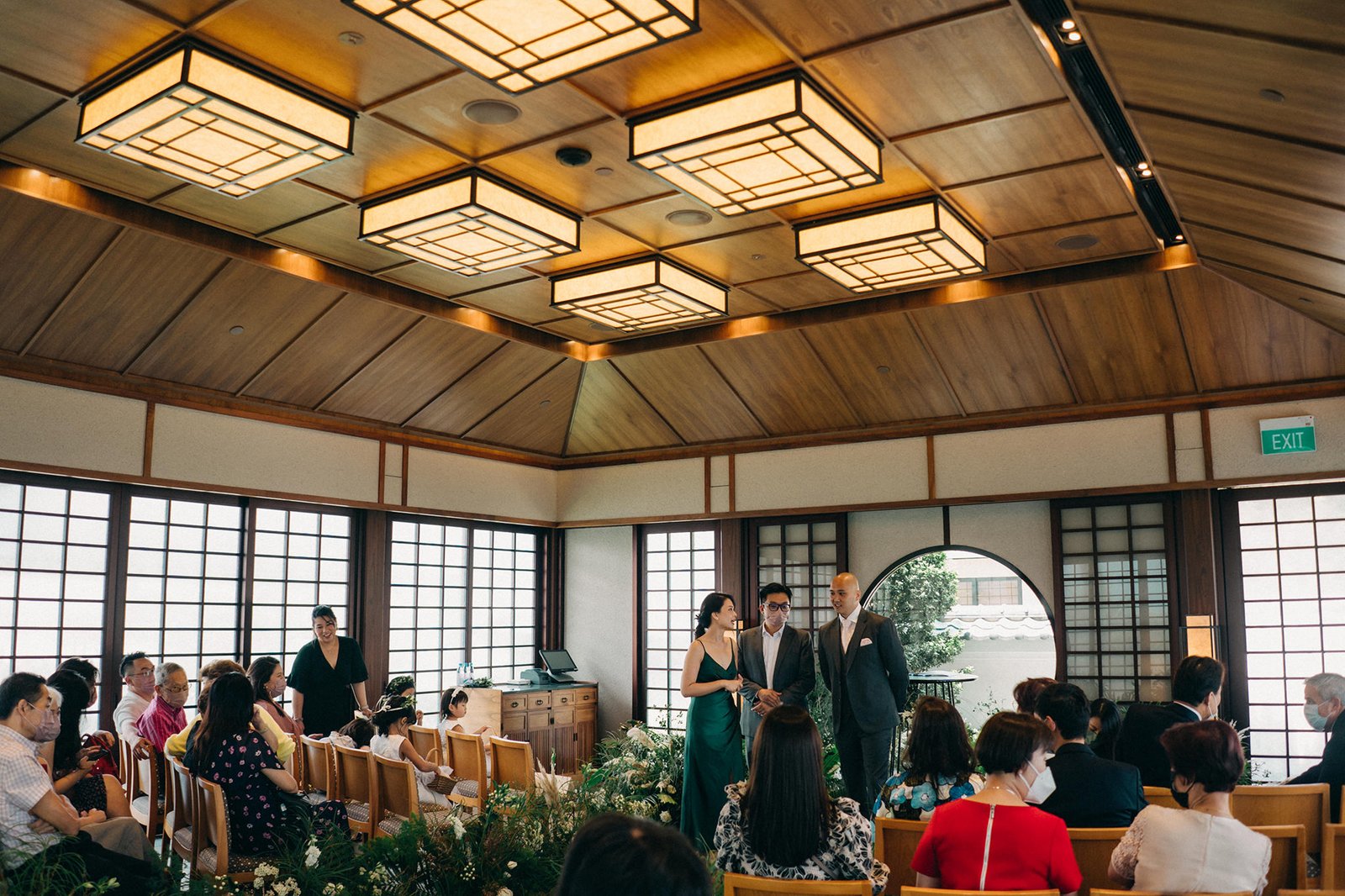 Kin + Christine's intimate Keyaki Garden Pavilion wedding ceremony in Singapore, with guests seated as the officiant, bride in green, and groom in a suit stand at the front.