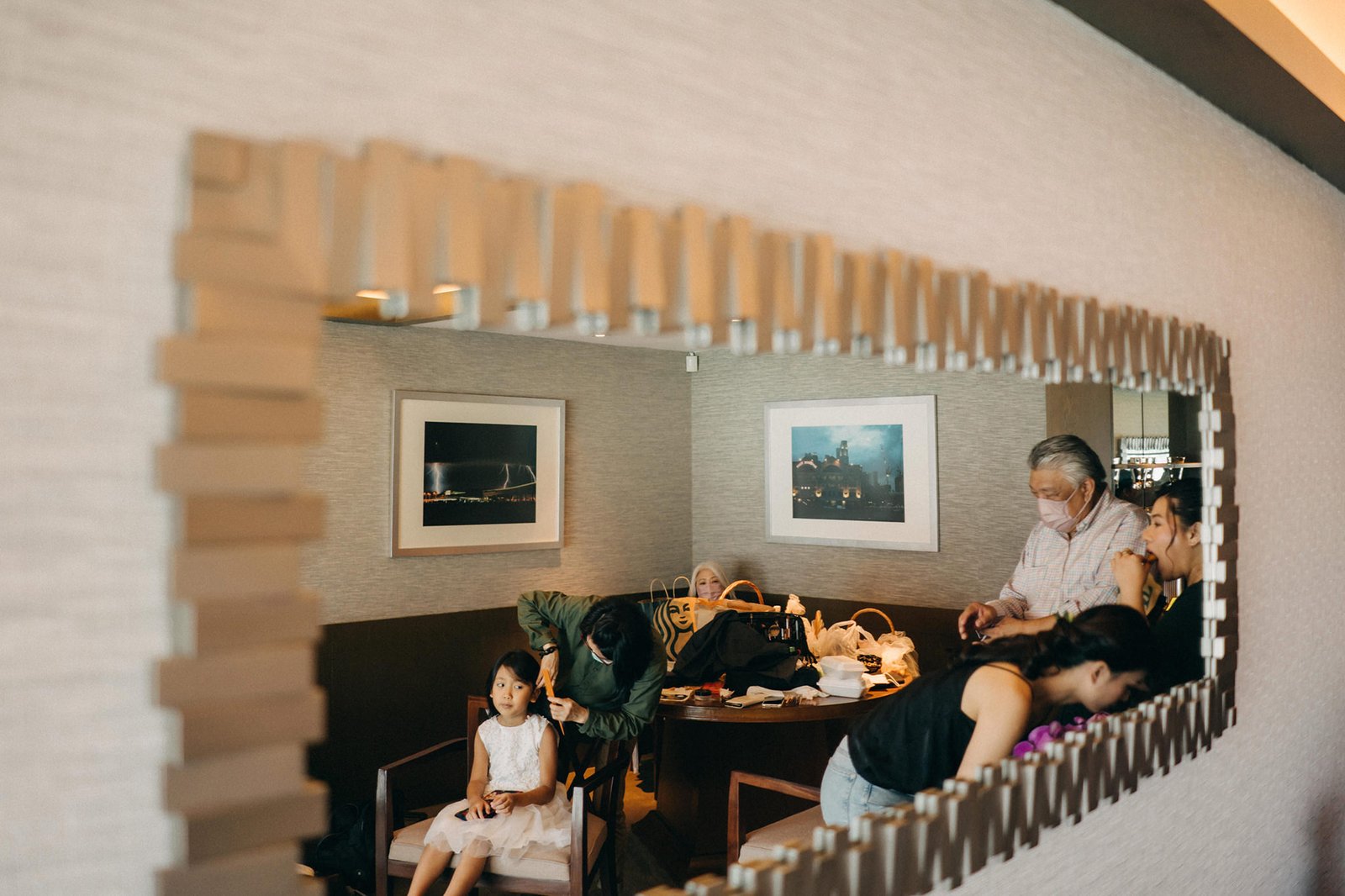 A wedding preparation scene at Keyaki Garden Pavilion, Singapore, with a young girl in a white dress seated, while several adults are gathered around a table, getting ready.