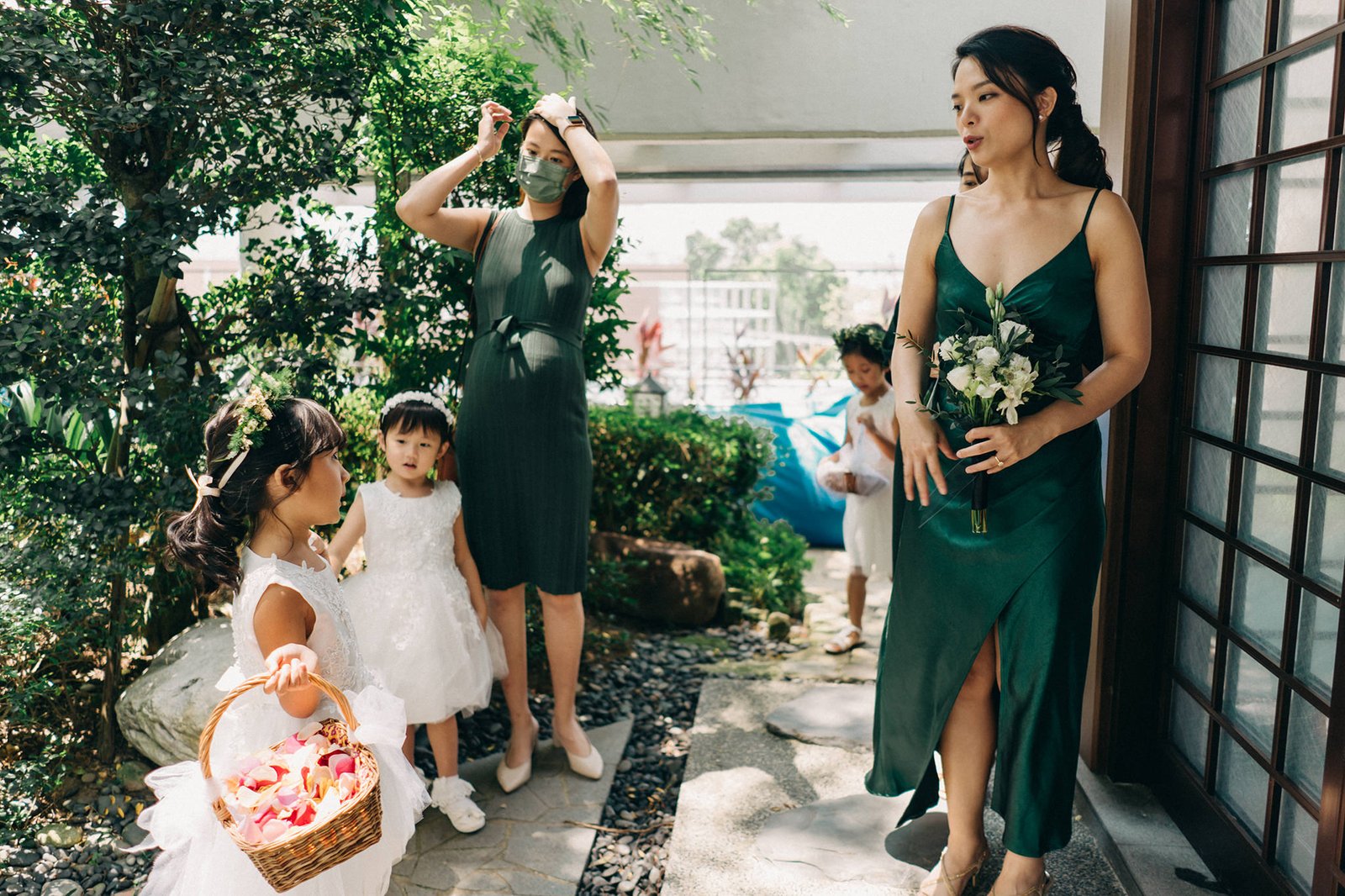 A wedding party in emerald green and white dresses, including flower girls, gathers outdoors at a Keyaki Garden Pavilion Wedding Singapore.