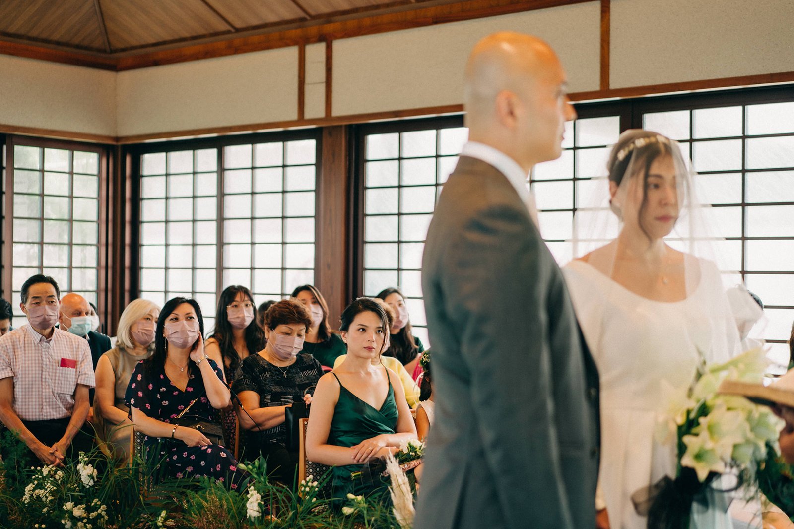 Kin and Christine's intimate wedding ceremony at Keyaki Garden Pavilion, Singapore, with guests wearing masks attentively watching the bride and groom.