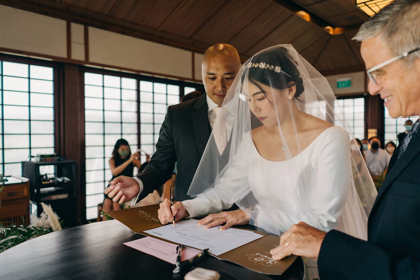 Bride and groom sign wedding certificate at Keyaki Garden Pavilion Wedding Singapore, officiant looking on.