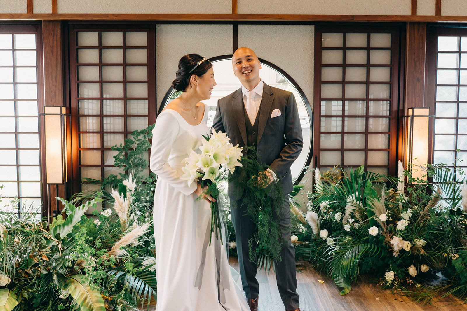 Kin and Christine smile at each other during their Keyaki Garden Pavilion wedding in Singapore, surrounded by lush greenery and white lilies.