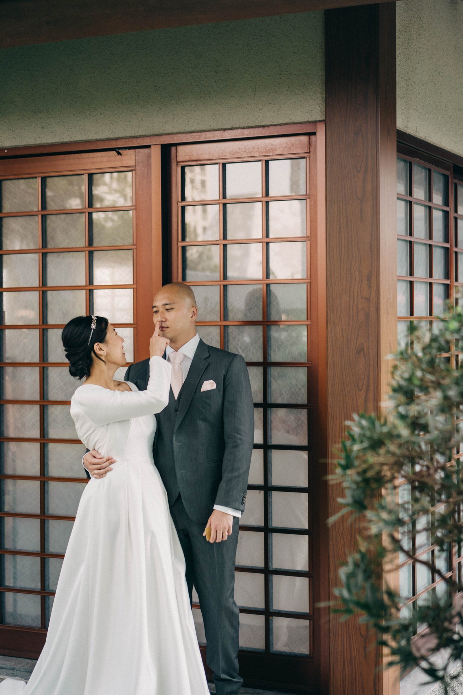 Bride in a white gown touches groom's face in front of traditional Japanese doors at Keyaki Garden Pavilion, Singapore wedding.