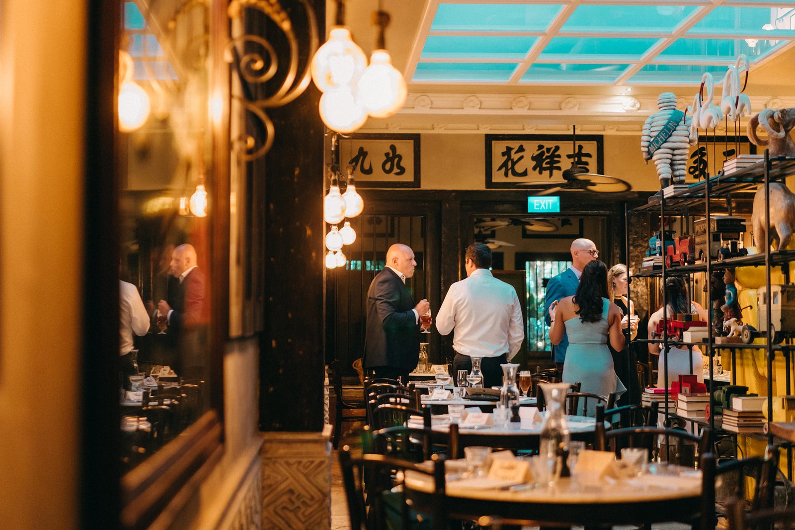 Guests mingle at a wedding reception at The English House Singapore, with warm lighting and ornate decor.