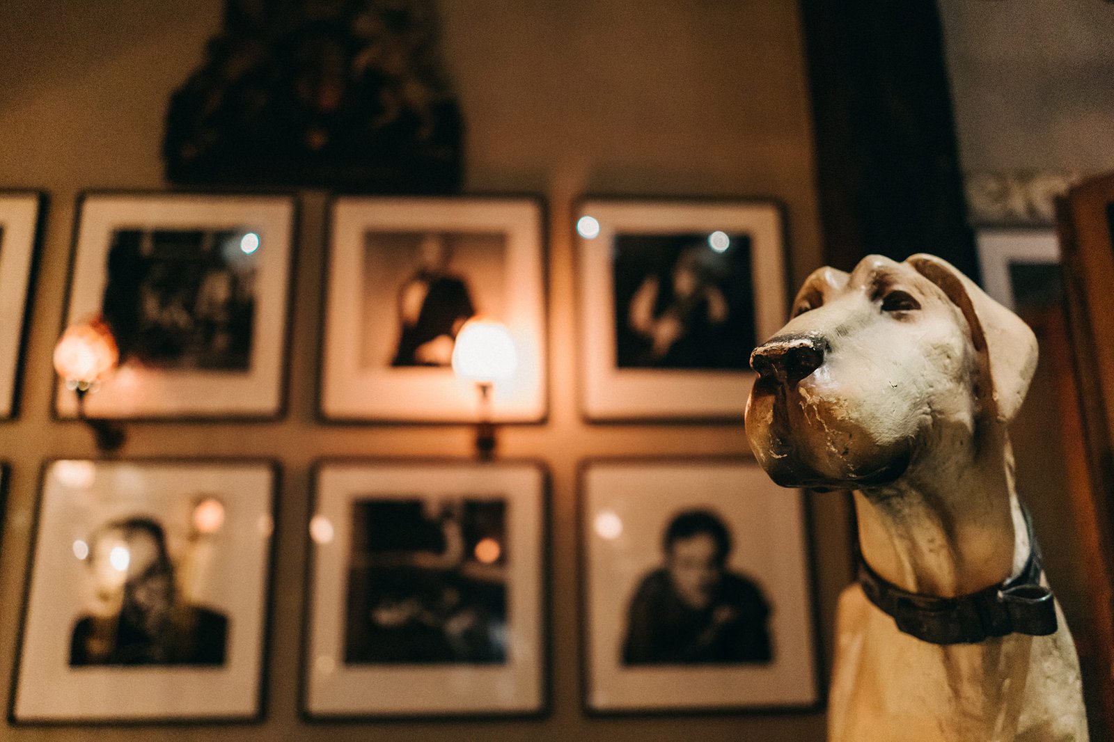 A vintage-style dog statue sits in the foreground, looking to the right, with a wall of framed black and white photos in the background. This scene could be part of a wedding at The English House Singapore.