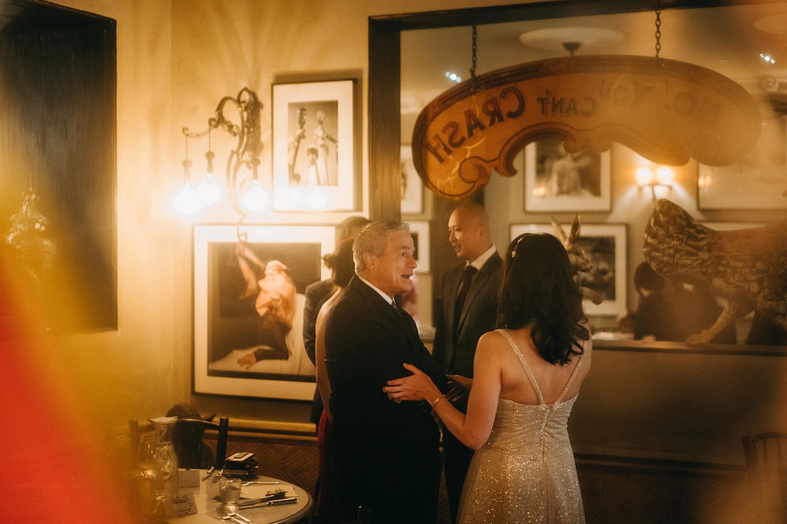 A wedding reception at The English House Singapore, with guests mingling in a warmly lit, elegant room featuring framed artwork and a vintage sign.
