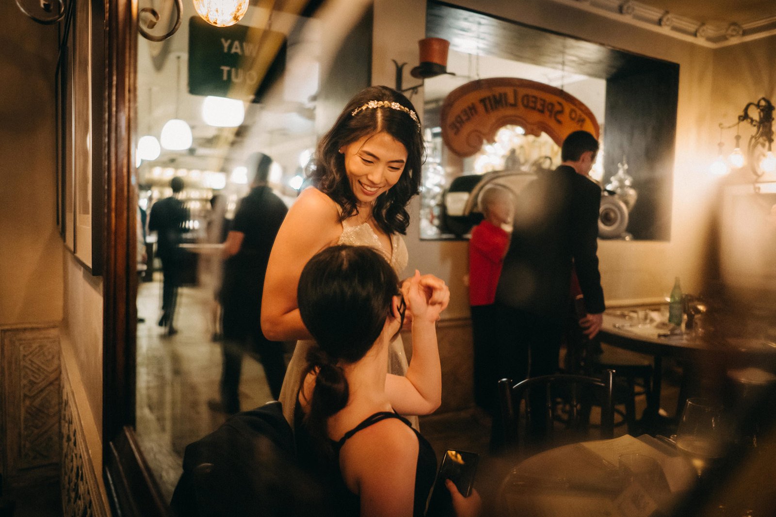 A bride with a floral headband smiles at a child at The English House wedding in Singapore, with reflections of the restaurant's interior visible.