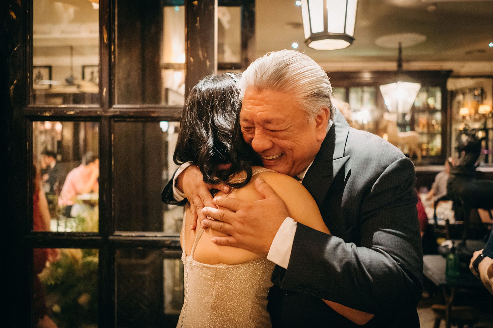 A groom embraces his bride at The English House Wedding Singapore, both beaming with joy. The bride wears a sparkling gown, and the groom is in a dark suit.