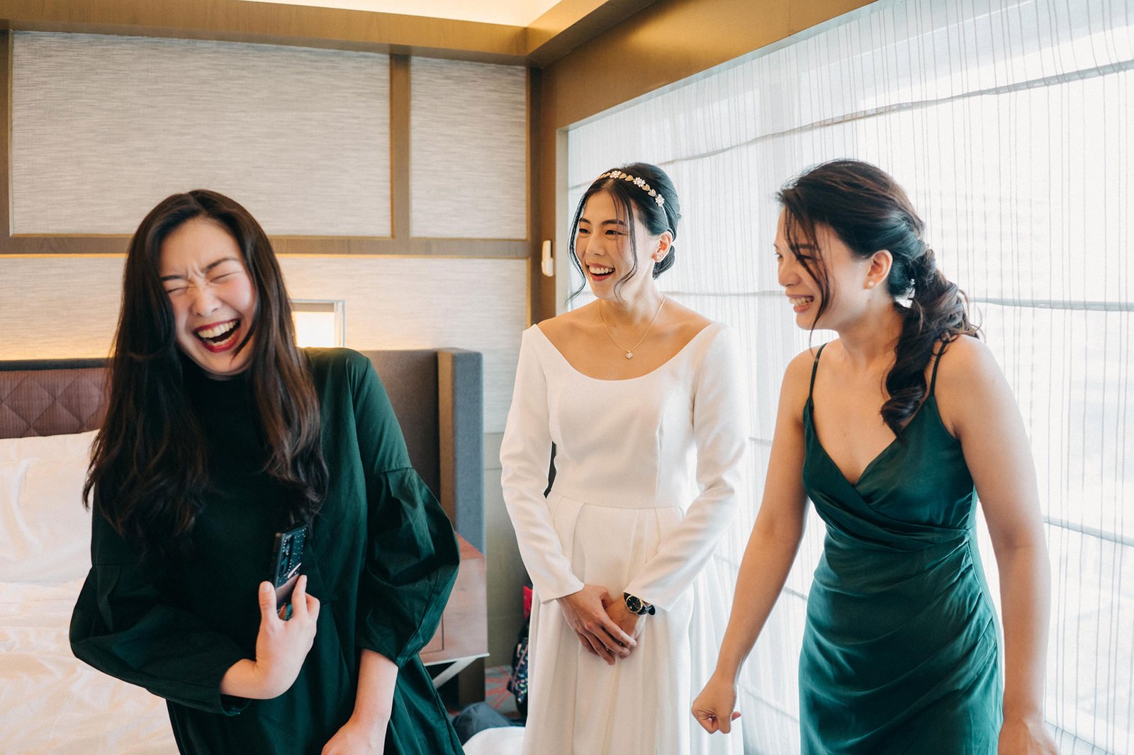 A bride in a white dress laughs with her bridesmaids in elegant green dresses, getting ready for a wedding at Keyaki Garden Pavilion Singapore.
