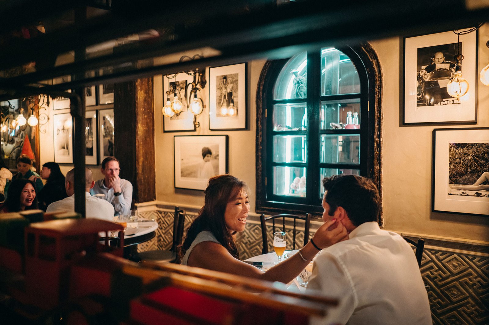 A happy couple shares an intimate moment over dinner at The English House Singapore, surrounded by eclectic decor and framed photographs, hinting at a wedding celebration.