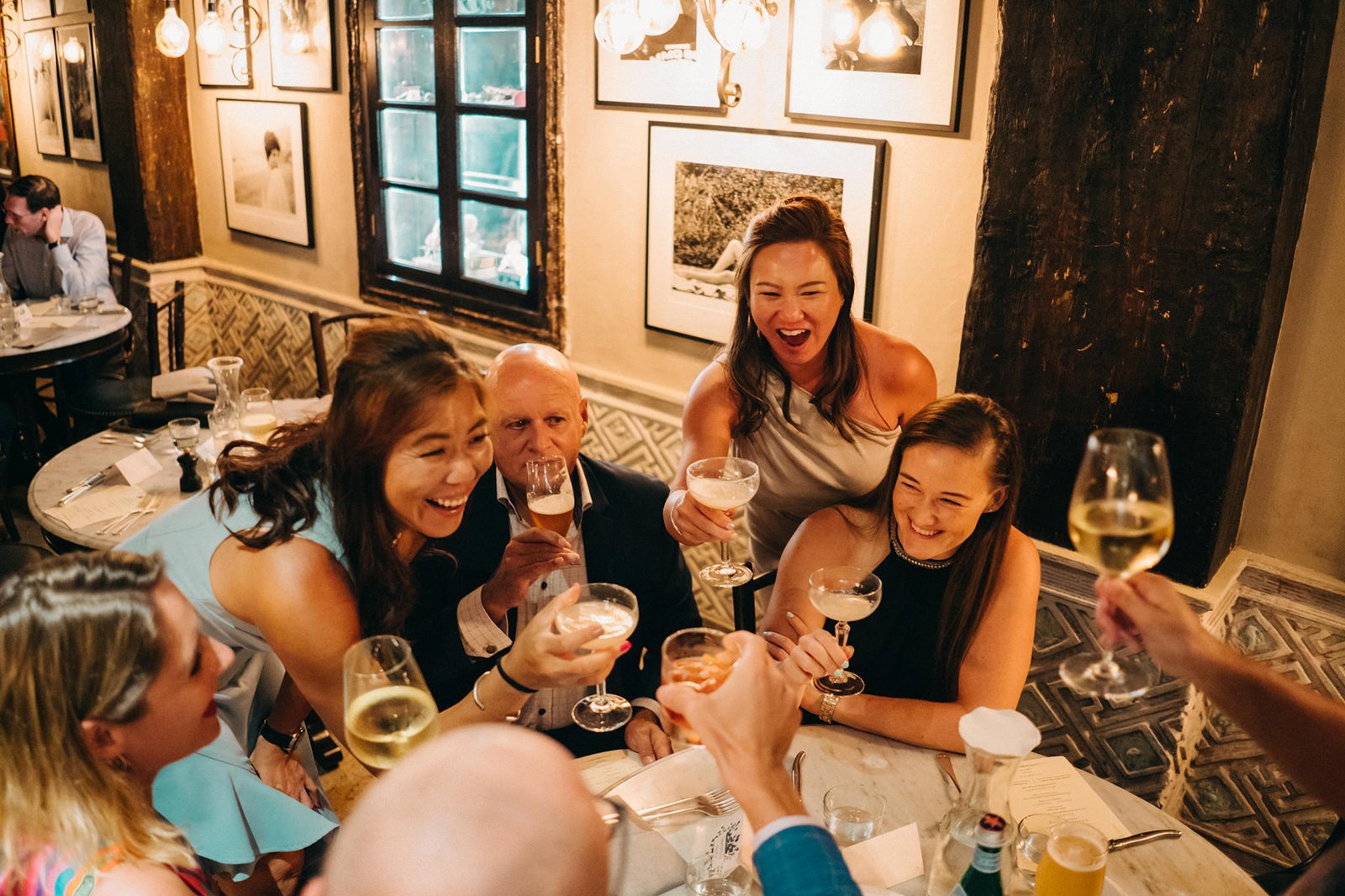 A joyous wedding toast at The English House Singapore, with guests raising champagne glasses and laughing during a Cacio e Pepe celebration.