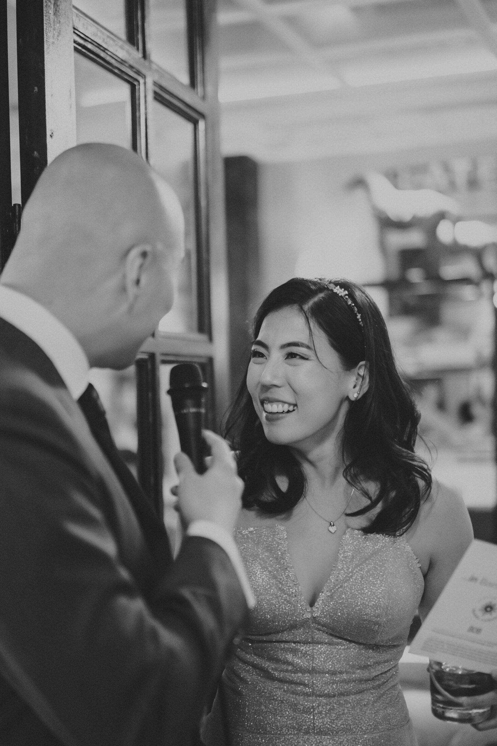 A beaming bride in a sparkly dress and a microphone-holding groom share a joyful moment at The English House Wedding Singapore.