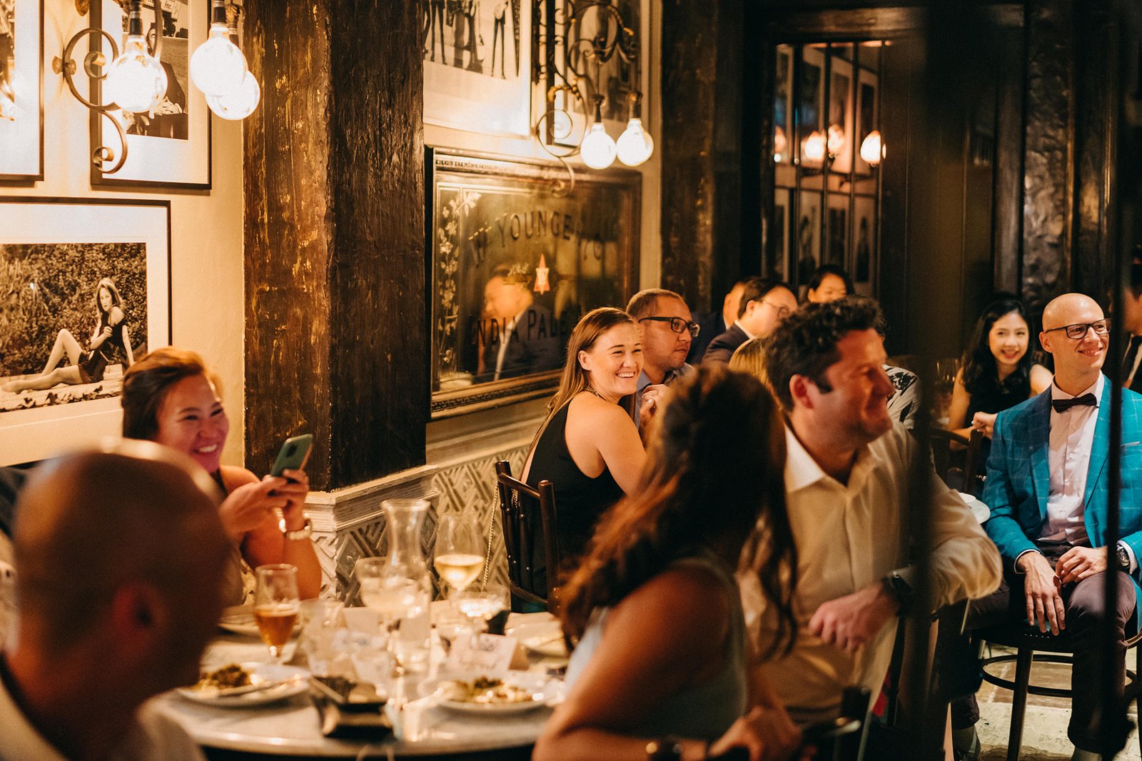 A lively wedding reception at The English House Singapore, with guests enjoying a meal and conversation, illuminated by warm, ambient lighting.