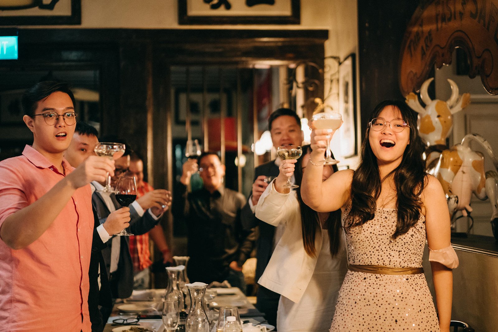 A group of people joyfully raise champagne glasses in a toast at a wedding celebration, possibly at The English House Wedding Singapore.