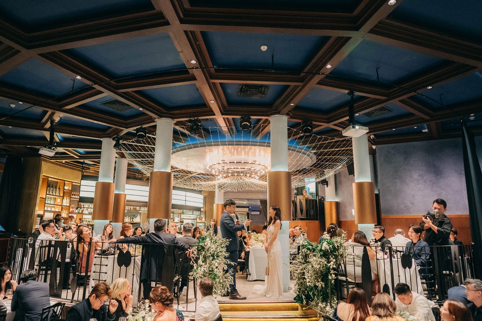 Wedding ceremony at Monti at 1-Pavilion Singapore, with a bride and groom exchanging vows under a stunning chandelier, surrounded by guests and floral arrangements.