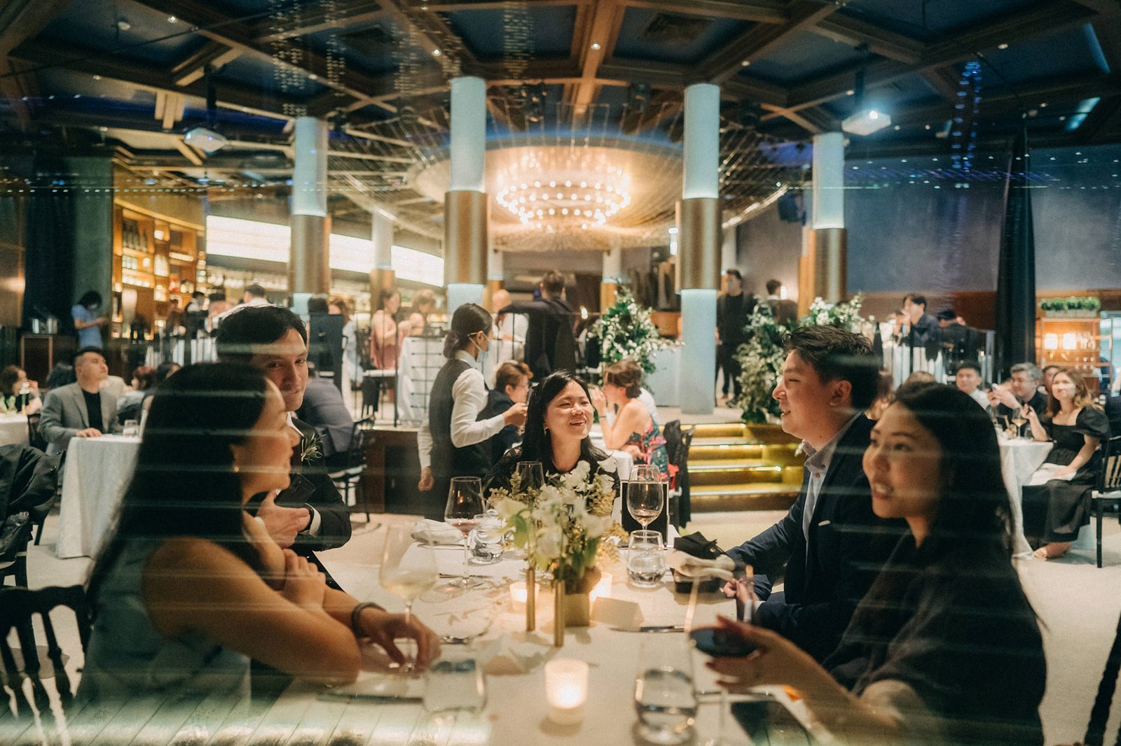 LK + Sophie's wedding reception at Monti at 1-Pavilion, Singapore, with guests dining at elegantly set tables under a grand chandelier.
