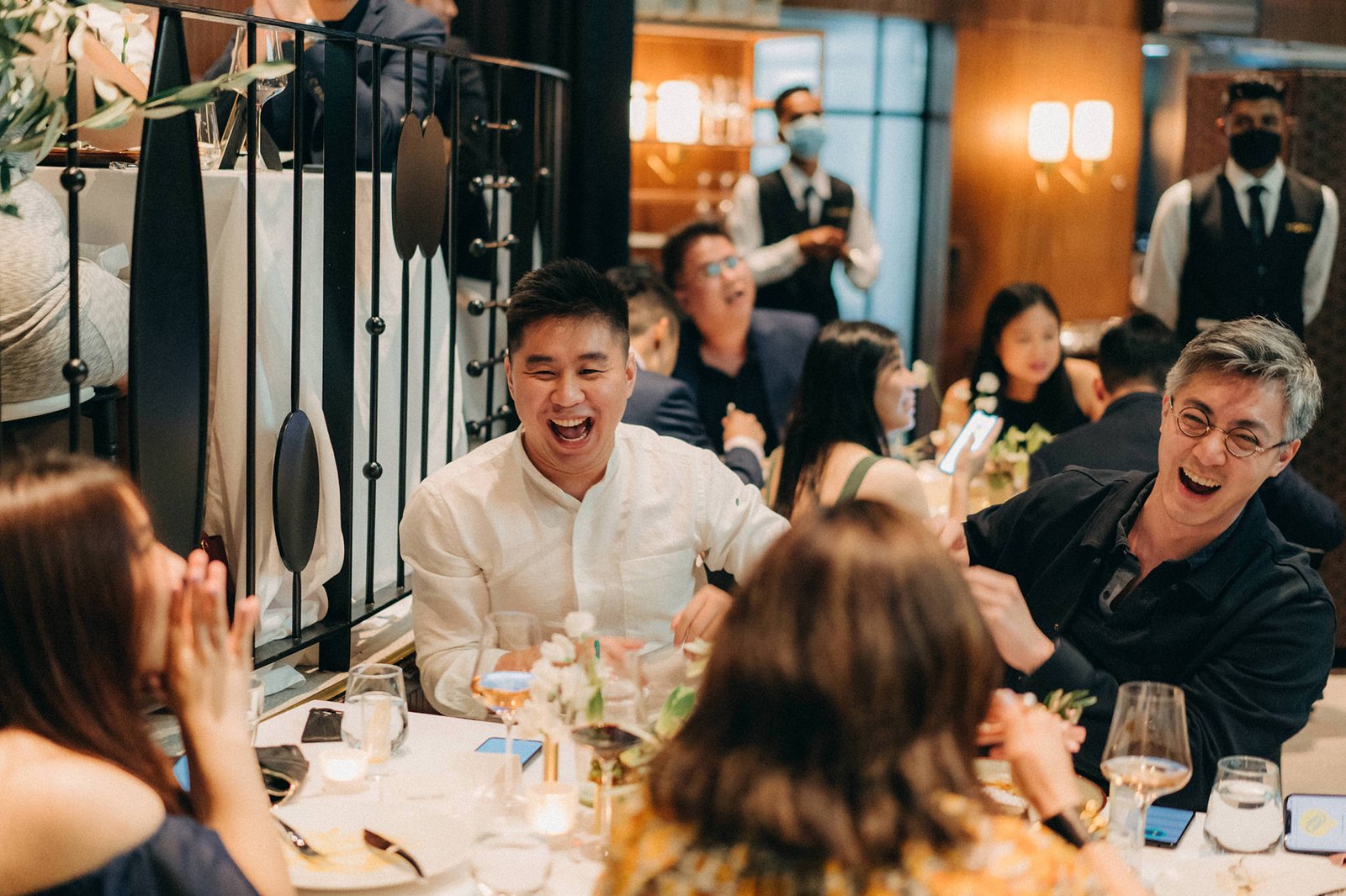 Joyful guests laugh at a wedding reception at Monti at 1-Pavilion in Singapore, captured by wedding photography.