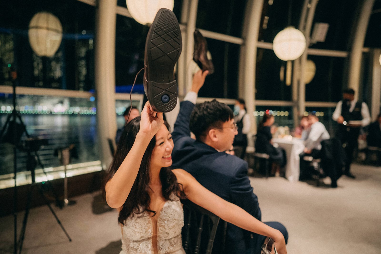 Bride and groom at Monti at 1-Pavilion wedding in Singapore, holding up shoes during a reception celebration. A lively wedding reception scene at Monti at 1-Pavilion in Singapore, with the bride and groom joyfully holding up their shoes during the festivities. This Monti at 1-Pavilion wedding photography captures a fun moment.