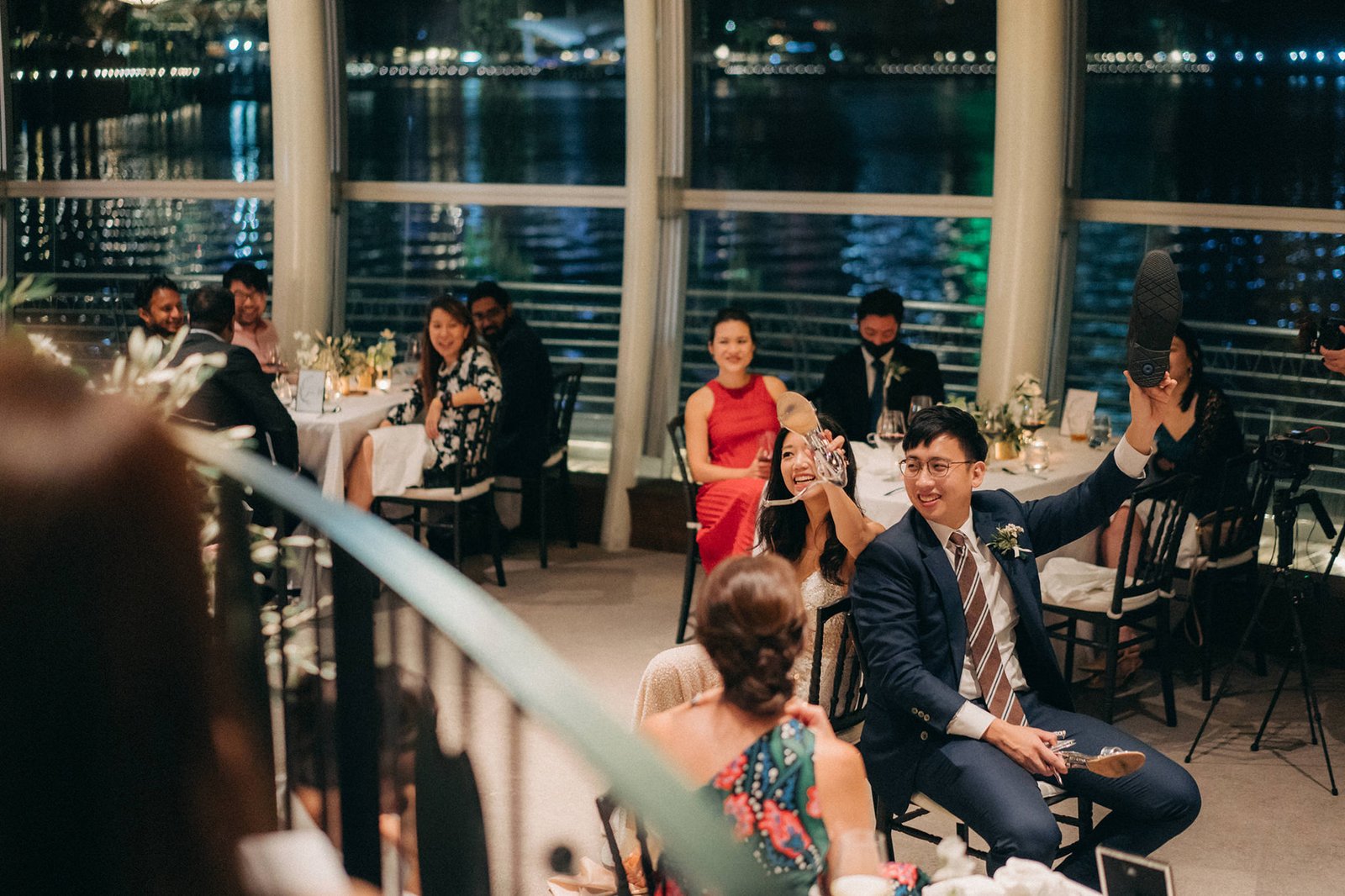 Wedding guests at Monti at 1-Pavilion, Singapore, enjoy a reception with a man in a suit holding up a shoe, smiling at the camera. The Monti at 1-Pavilion wedding photography captures the joyful atmosphere.