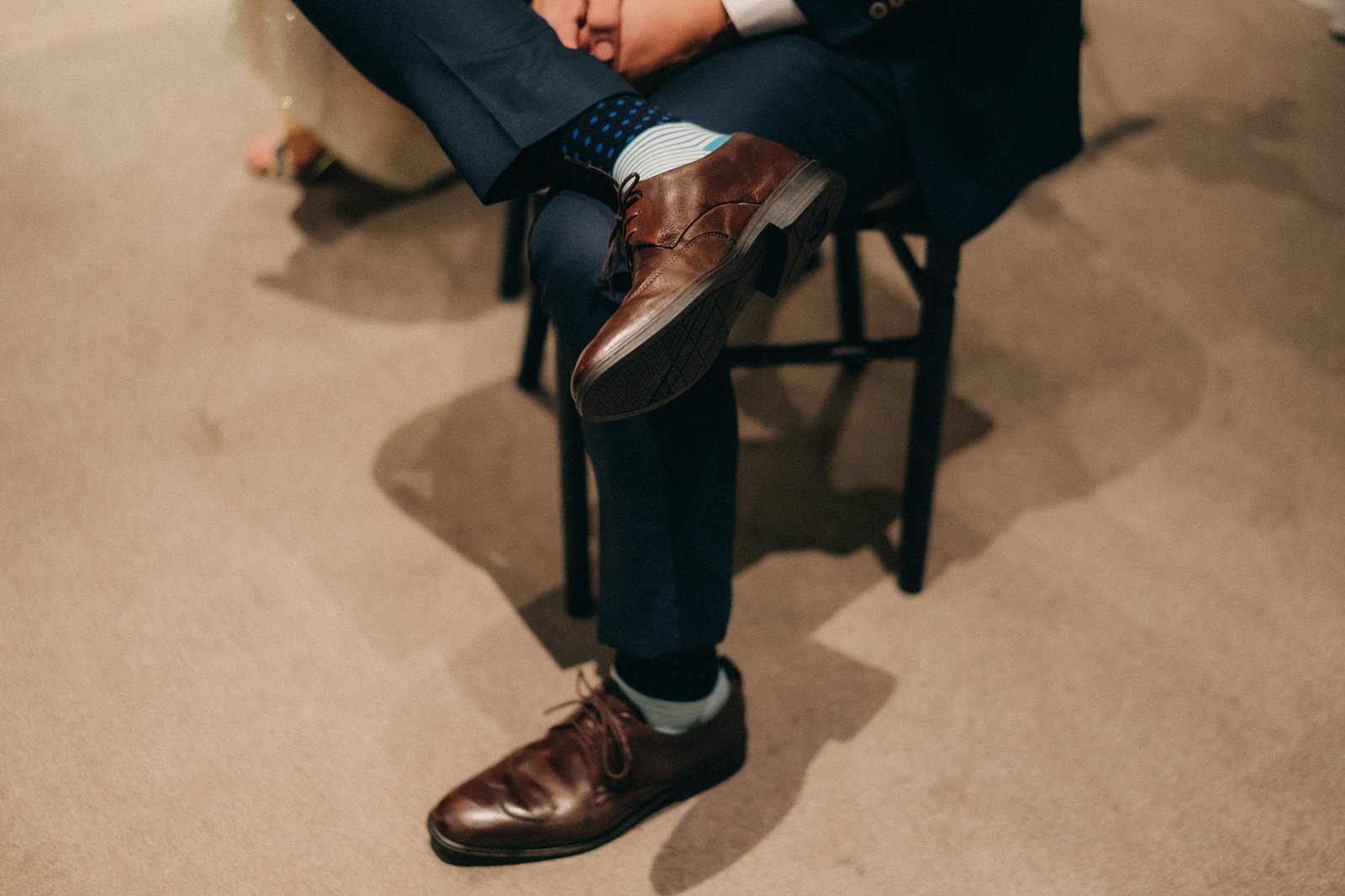 Groom's brown dress shoes and patterned socks are visible as he sits, with a hint of a navy suit, at a Monti at 1-Pavilion wedding in Singapore.