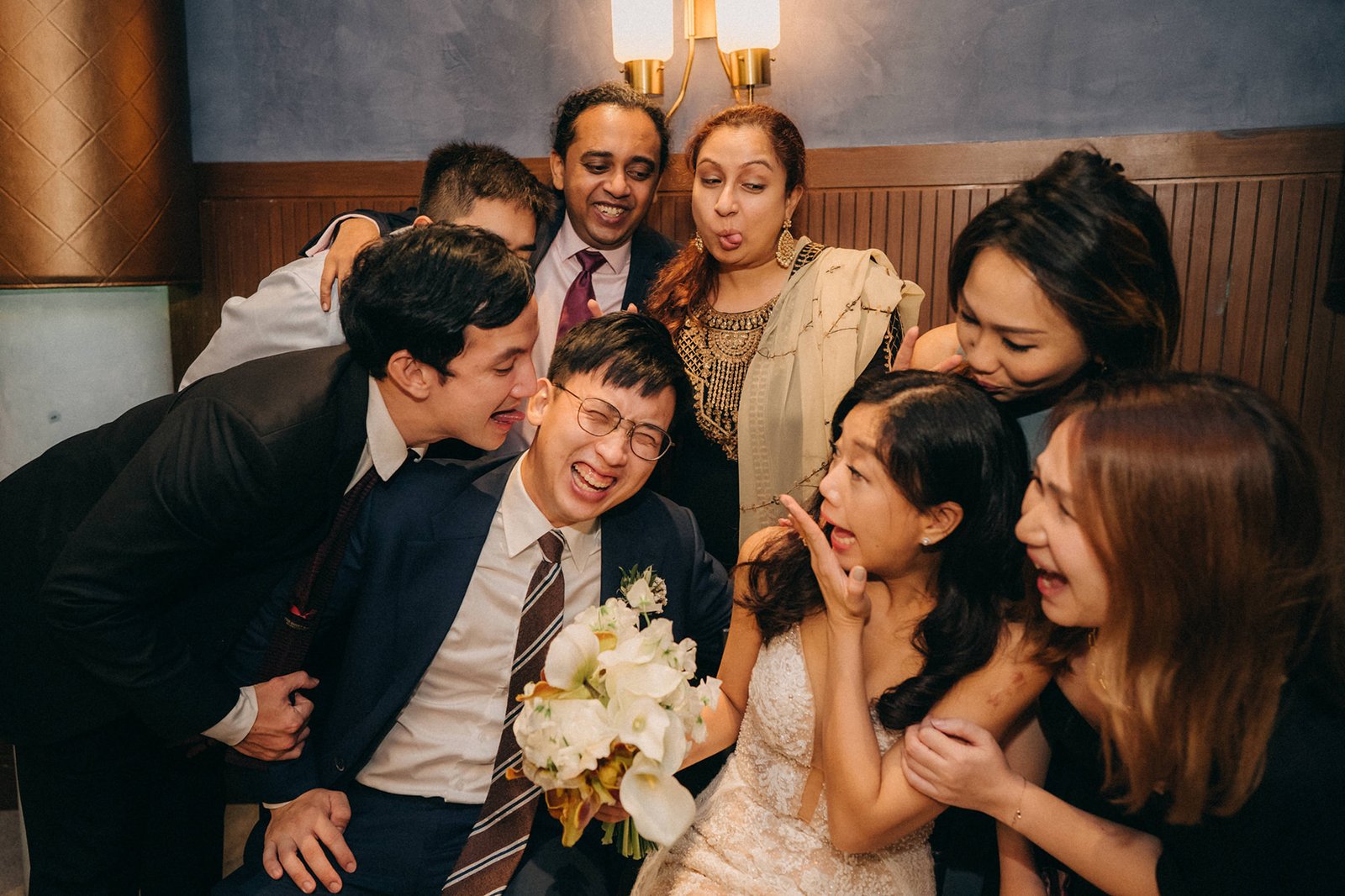 A joyous wedding party playfully poses for a photo at Monti at 1-Pavilion, Singapore, with the bride and groom in the center surrounded by friends and family making funny faces. This Monti at 1-Pavilion wedding photography captures the fun atmosphere.