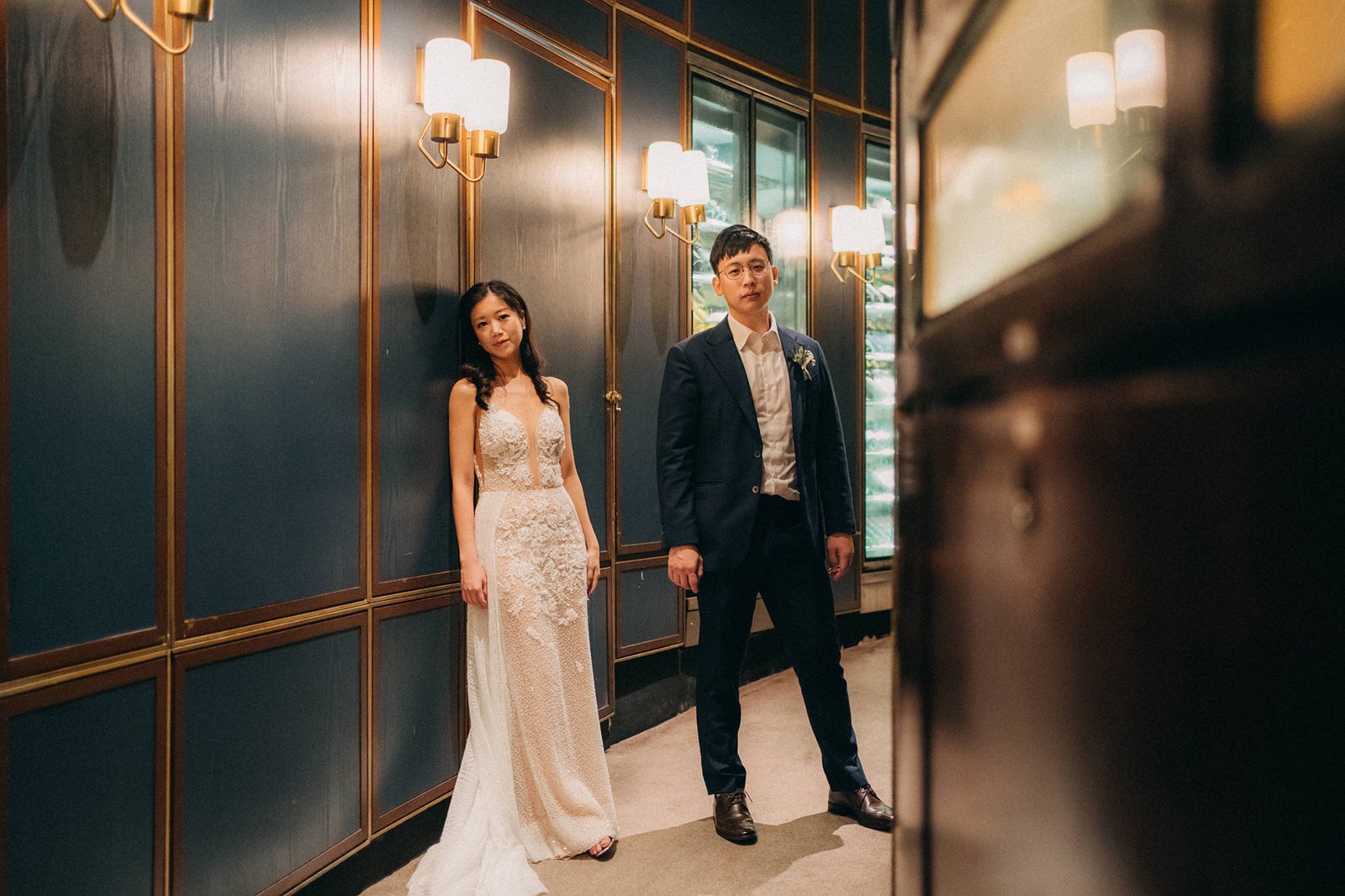 A bride in a white lace gown and a groom in a navy suit pose for wedding photography at Monti at 1-Pavilion in Singapore.