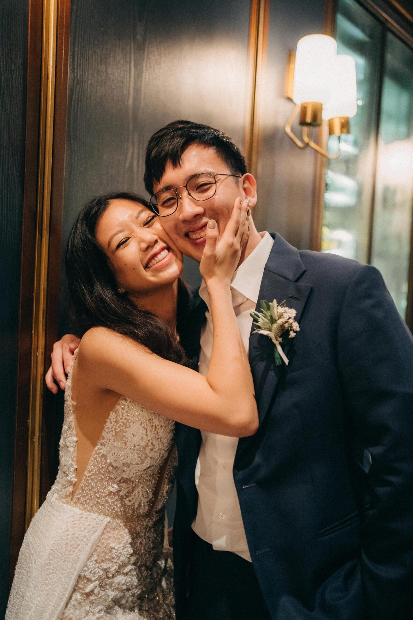 A joyful bride in a sparkling white gown embraces her groom in a dark suit, both smiling warmly at a Monti at 1-Pavilion wedding in Singapore, captured by photography.