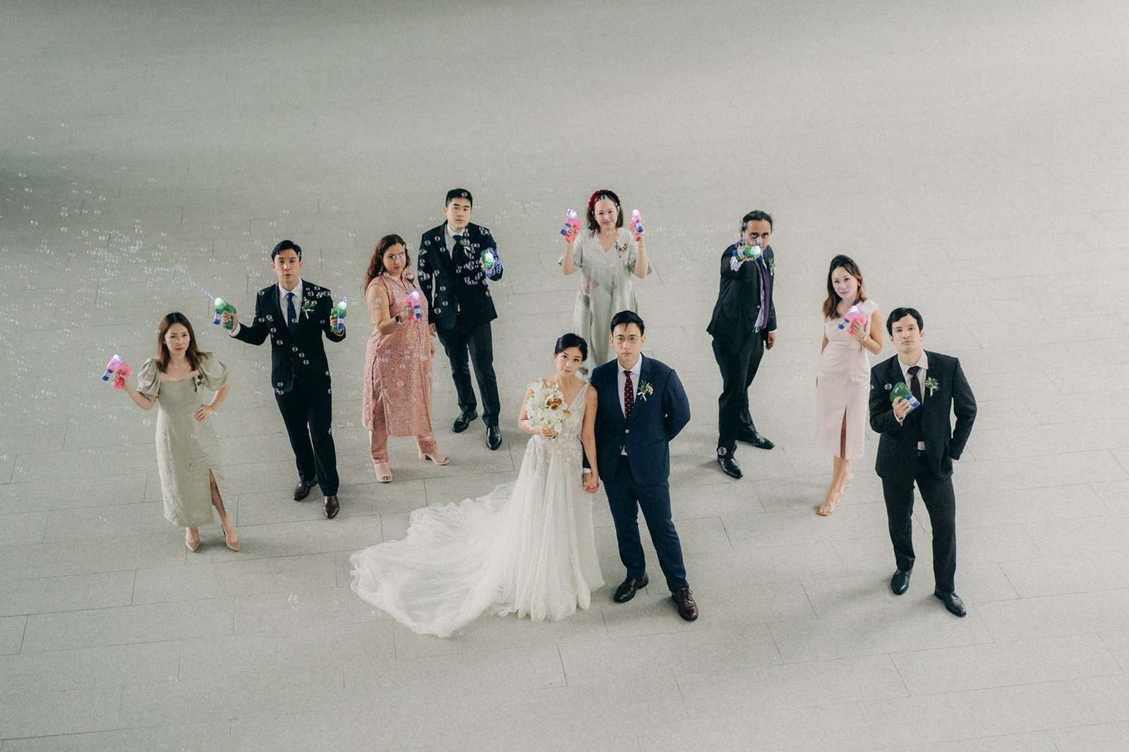 Wedding party at Monti at 1-Pavilion, Singapore, holding bubble guns. Bride in a white gown, groom in a navy suit, with bridesmaids and groomsmen in festive attire. A joyous celebration captured by Monti at 1-Pavilion wedding photography.