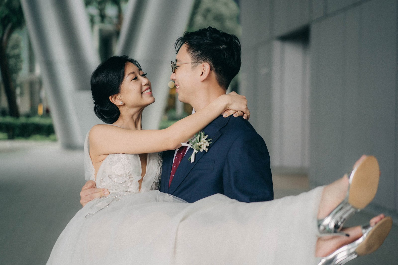 Groom carries bride at Monti at 1-Pavilion, Singapore, a romantic wedding photography moment. The bride in a white gown smiles at her groom in a navy suit.
