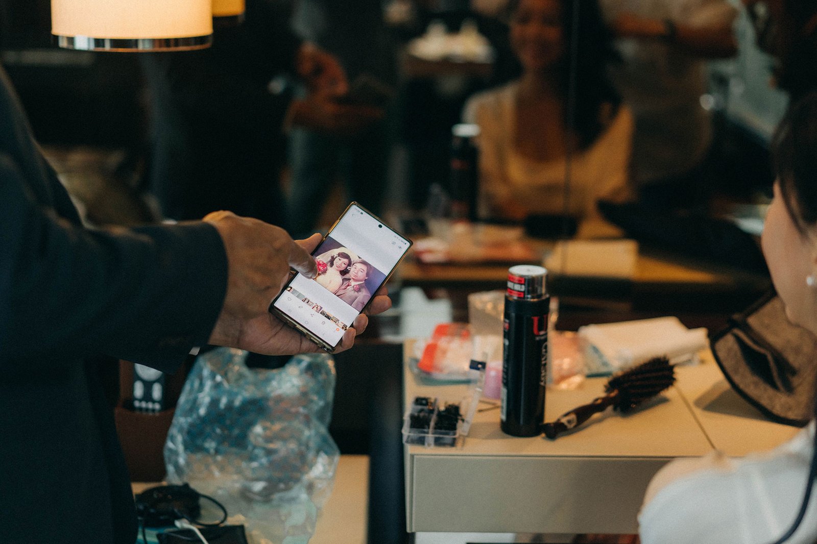 A wedding photographer in Singapore captures a moment at Monti at 1-Pavilion, showing a phone displaying a couple's photo, with wedding preparations in the background.
