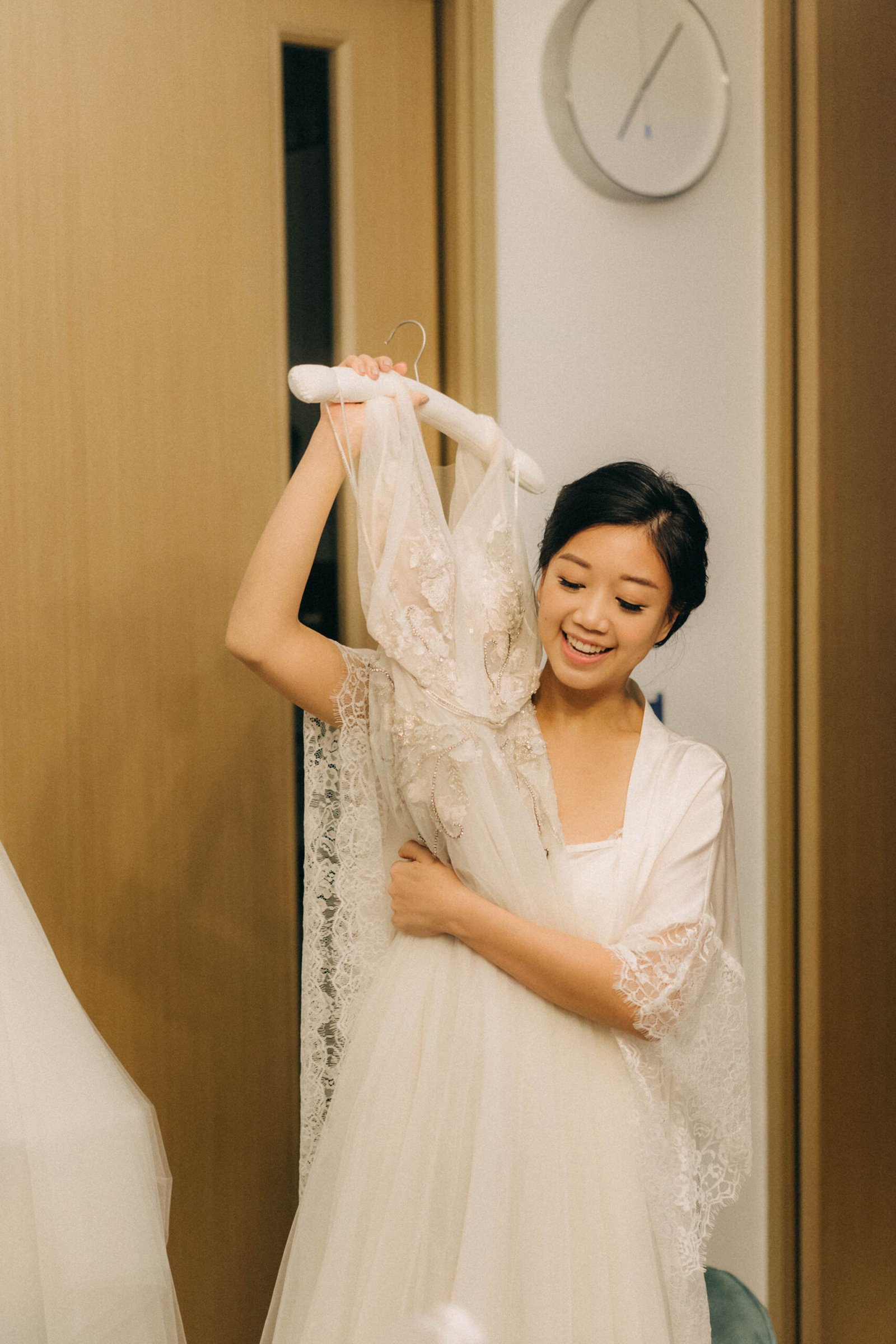 Bride smiling, holding up her intricate lace wedding dress before her wedding at Monti at 1-Pavilion, Singapore.