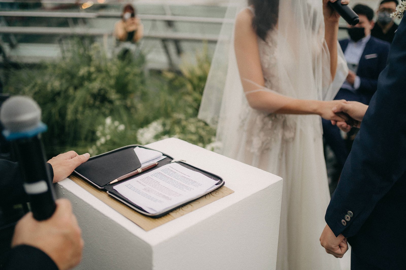 A bride and groom hold hands during an intimate wedding ceremony at Monti at 1-Pavilion, Singapore, with officiant and guests in the background. Photography by [Your Photography Name].