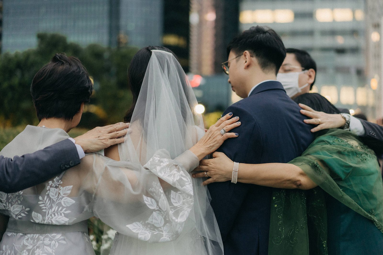 Wedding photography at Monti at 1-Pavilion, Singapore: A bride and groom are embraced by family, sharing a tender moment during their wedding celebration.