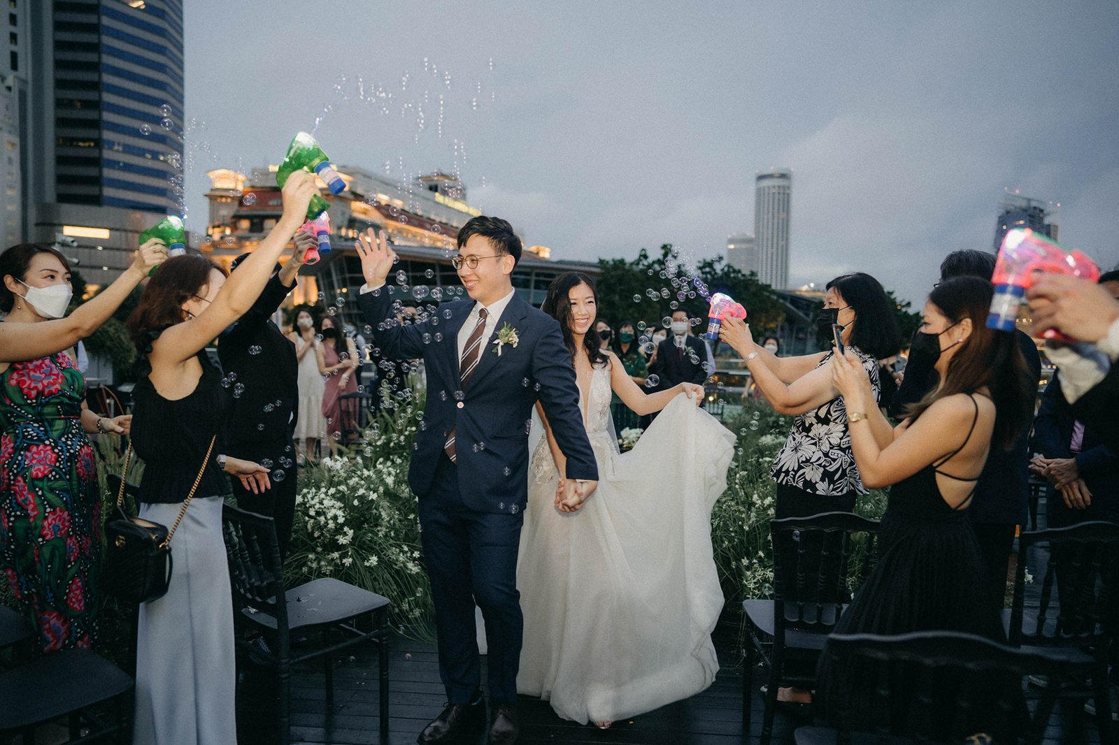 A happy bride and groom walk through a bubble send-off at their Monti at 1-Pavilion wedding in Singapore, captured by photography.