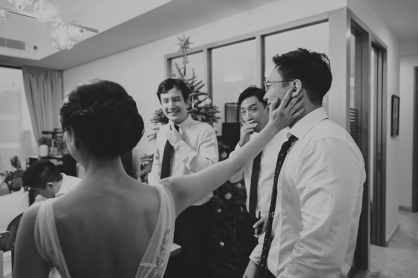 A candid black and white wedding photo at Monti at 1-Pavilion, Singapore, shows a bride touching the groom's face as he smiles, with groomsmen in the background. Monti wedding photography.