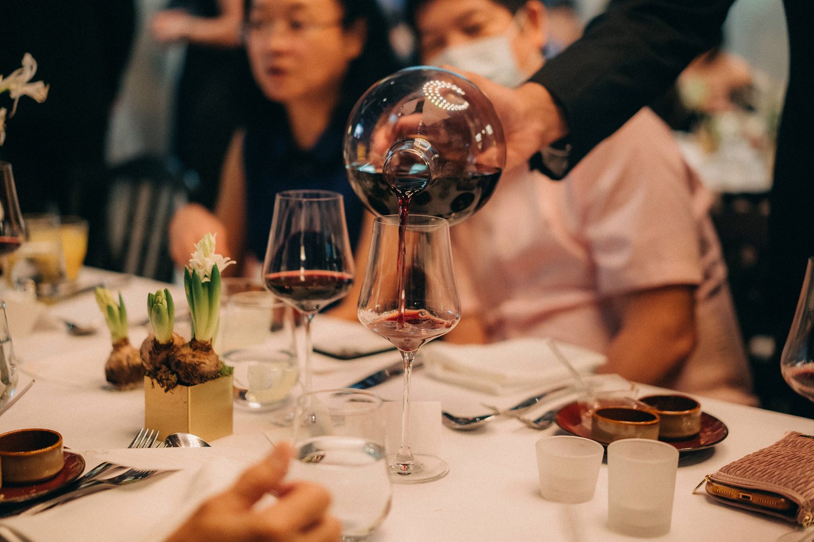 A server pours red wine into a glass at a Monti Circles wedding reception in Singapore, with guests dining at elegantly set tables.