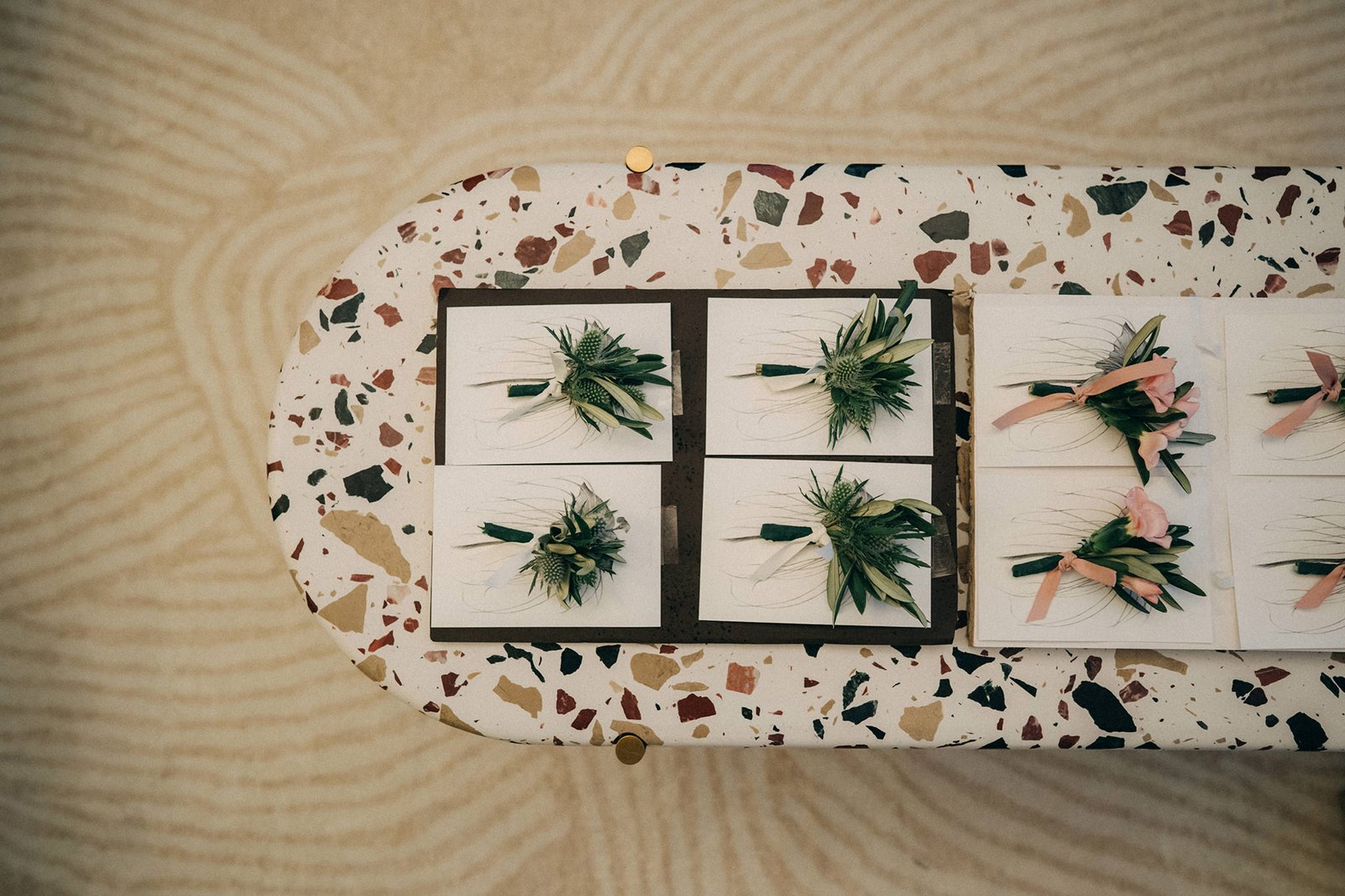 Close-up of delicate wedding boutonnieres with greenery and pink flowers, arranged on white cards on a terrazzo table at Monti at 1-Pavilion, Singapore.
