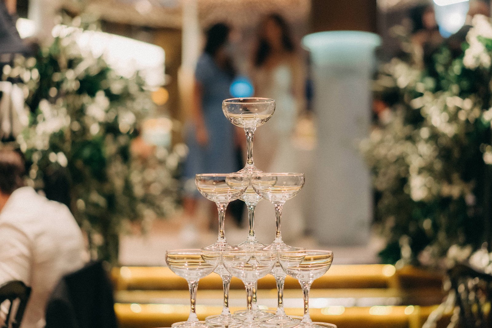 A champagne tower at a Monti at 1-Pavilion wedding in Singapore, with blurred guests and lush greenery in the background.