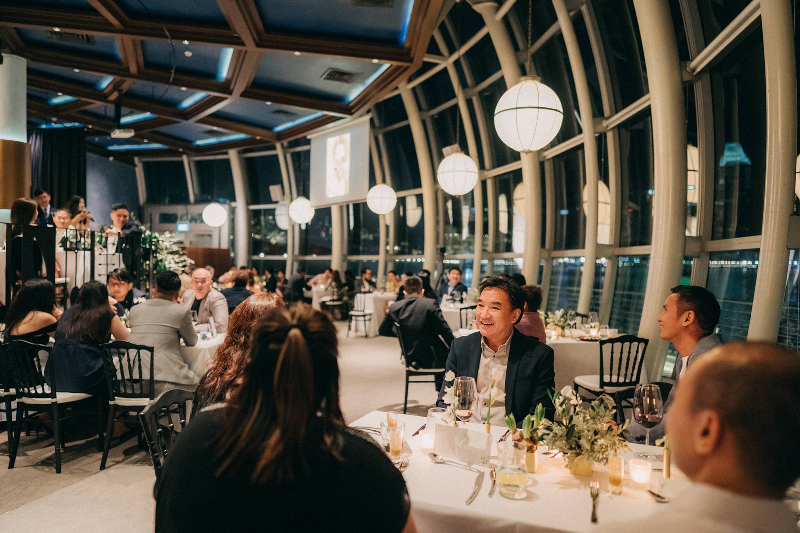 A wedding reception at Monti at 1-Pavilion, Singapore, with guests seated at elegantly set tables under a modern ceiling with circular lights.