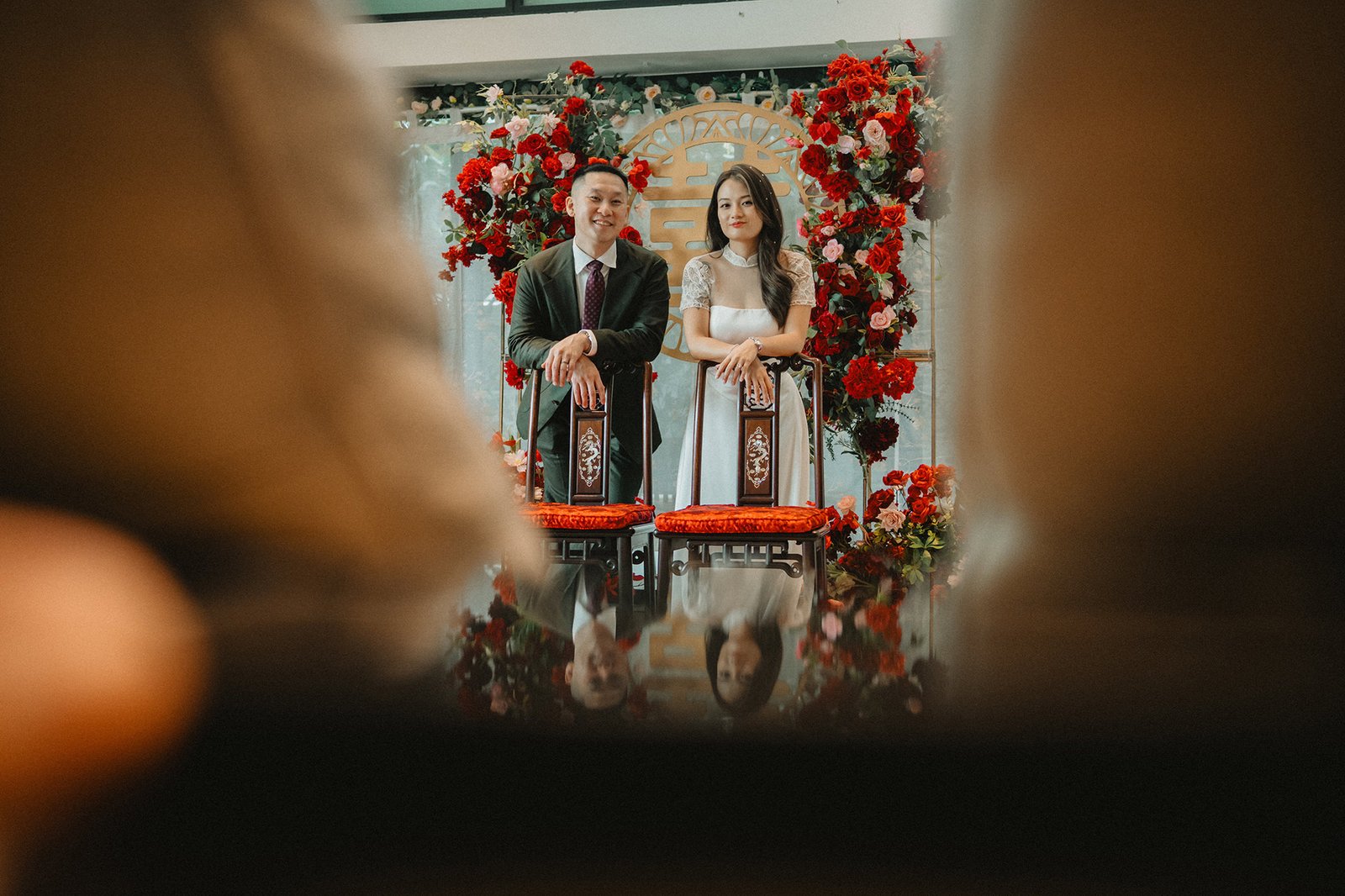 Jared and Xinyu wedding at Atlas Bar Singapore, seated amidst red floral decor.