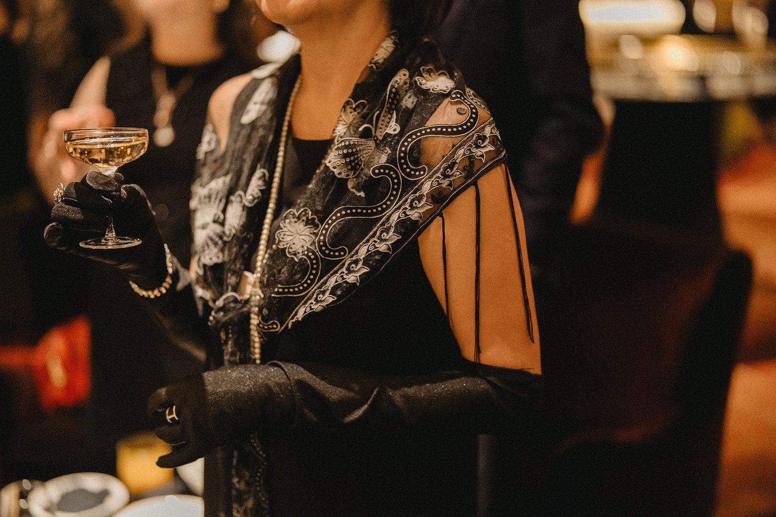 Elegant woman in black dress and gloves holds champagne at Atlas Bar Singapore wedding.